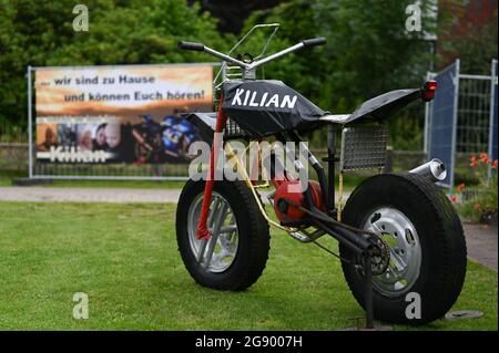 Leer, Germany. 23rd July, 2021. A motorcycle sculpture stands in front of a house, on whose fence hangs a banner with the inscription '. we are at home and can hear you'. Hundreds of motorcyclists are expected on Saturday (24.07.2021) in the village in East Frisia, to make with a parade a seriously ill six-year-old boy a joy. The police are even preparing for several thousand bikers. Credit: Lars Klemmer/dpa /dpa/Alamy Live News Stock Photo