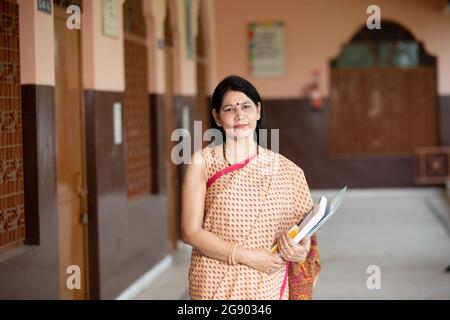 portrait of Smiling teacher in School corridor with books in hand Stock Photo