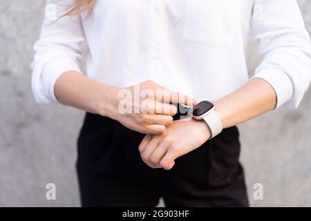 Young woman using smart watch while standing in front of wall Stock Photo