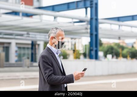 Businessman using smart phone at railroad station during pandemic Stock Photo