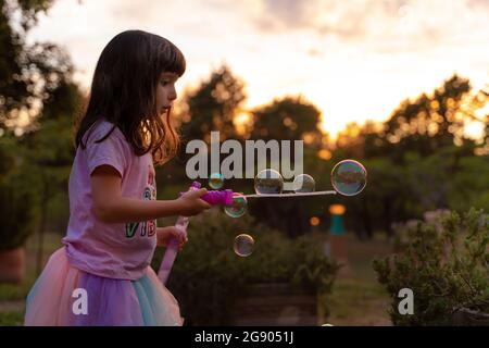 Girl playing with soap bubbles while holding wand during sunset Stock Photo