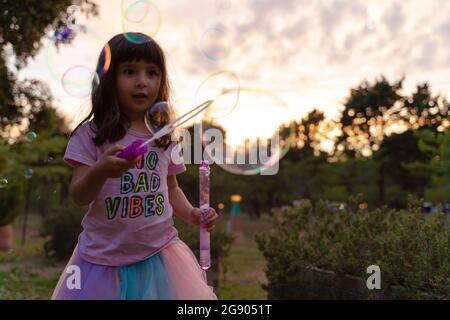 Girl looking with wand looking at soap bubbles while playing during sunset Stock Photo