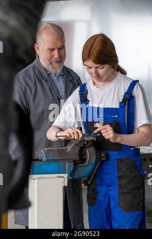 Female apprentice working with machinery while male instructor assisting in workshop Stock Photo