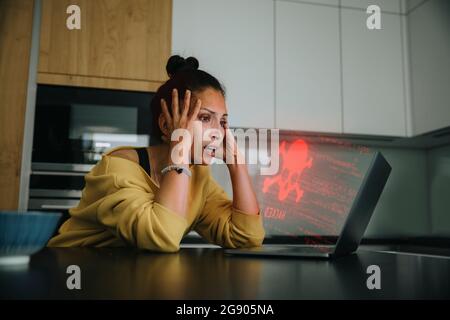 Woman with head in hands looking at danger icon laptop Stock Photo