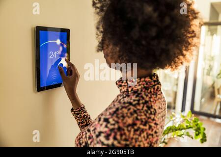 Woman adjusting temperature on smart thermostat at home Stock Photo