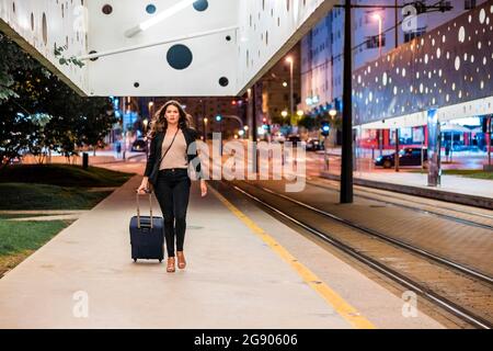 Businesswoman pulling wheeled luggage while walking on platform at night Stock Photo