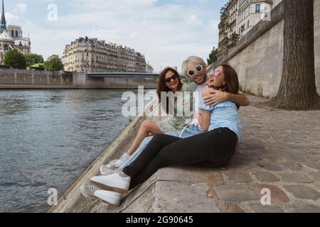 Male and female friends having fun while sitting at river Stock Photo