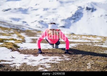 Female athlete doing push-ups on mountain during sunny day Stock Photo