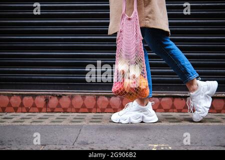 Woman with fruits in mesh bag walking by shutter Stock Photo