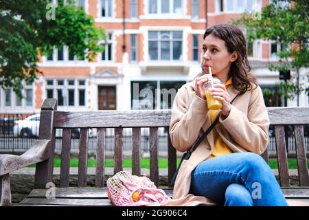 Young woman looking away while drinking smoothie on bench Stock Photo