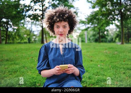 Beautiful young woman sitting with smart phone at park Stock Photo