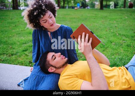 Young man reading book while lying on girlfriend lap at park Stock Photo