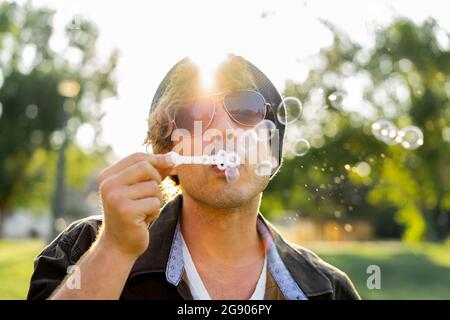 Young man wearing sunglasses blowing bubbles at park Stock Photo