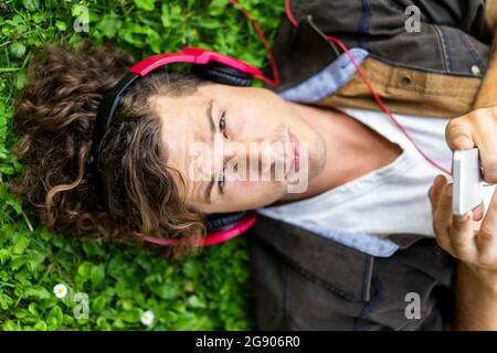 Young handsome man listening music through headphones lying on grass Stock Photo