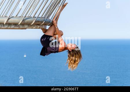 Cheerful mature woman hanging on railing stretching leg while practicing acrobatics at observation point Stock Photo
