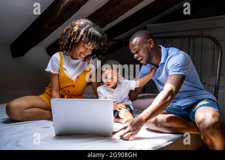 Happy family with son sitting on bed using laptop in attic at home Stock Photo