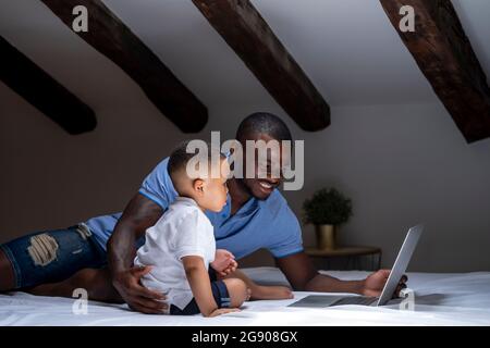Father using laptop with son on bed in attic at home Stock Photo