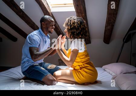 Romantic couple touching hands while sitting on bed in attic at home Stock Photo