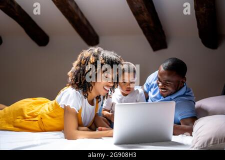 Smiling family using laptop with son while lying on bed at home Stock Photo