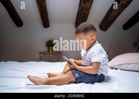 Boy using smart phone while sitting on bed at home Stock Photo