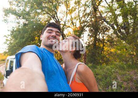 Woman kissing boyfriend while taking selfie at forest Stock Photo