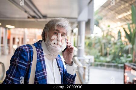 Mature man with white beard looking away while talking on smart phone at station Stock Photo