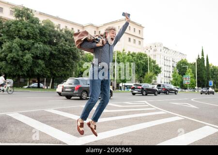 Excited mature man carrying luggage while jumping in joy on street Stock Photo