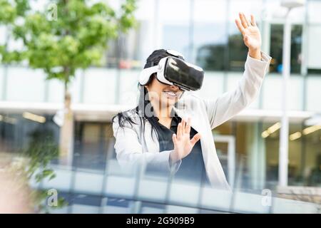 Businesswoman smiling while using virtual reality headset Stock Photo