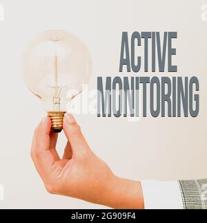 Hand writing sign Active Monitoring. Word Written on person incharge go out and check workplace conditions Hand holding lamp showing or presenting new Stock Photo