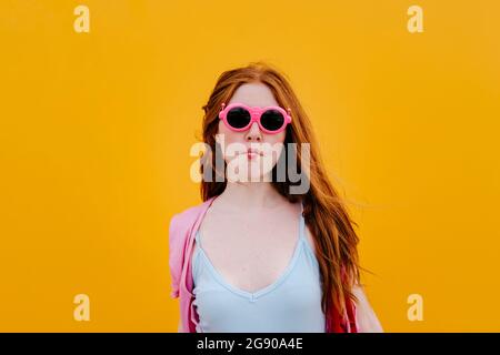 Redhead woman wearing sunglasses puckering in front of yellow wall Stock Photo