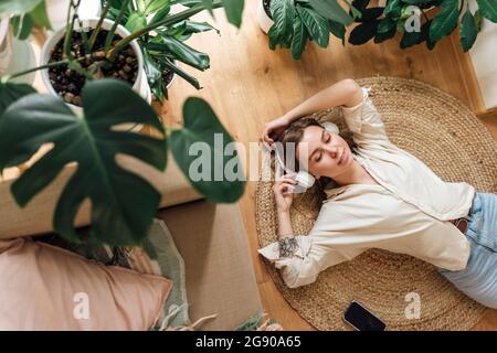 Woman with hands raised listening music while relaxing on rug at home Stock Photo