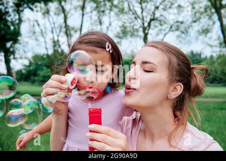 Daughter and mother blowing bubbles at park Stock Photo