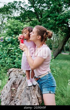 Mother and daughter blowing bubbles in park Stock Photo
