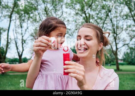 Cute daughter looking at mother holding bubble wand at park Stock Photo