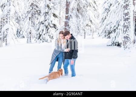 Young couple standing in snow with dog during vacation Stock Photo