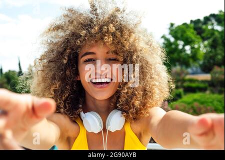 Cheerful curly haired woman wearing headphones on sunny day Stock Photo