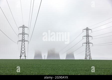 UK, England, Rugeley, Electricity pylons standing in field during foggy weather with cooling towers in background Stock Photo