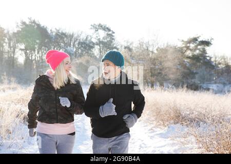 Active senior couple looking at each other while jogging on snow Stock Photo