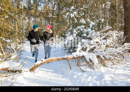 Active senior couple running on snow in forest during sunny day Stock Photo