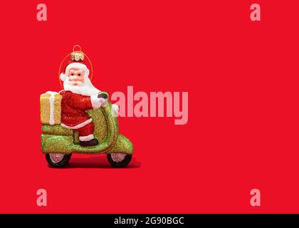 Christmas ornament of Santa Claus riding motor scooter against vibrant red background Stock Photo