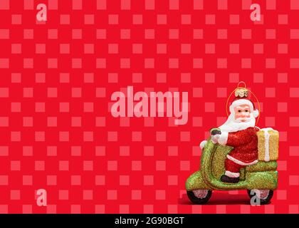 Christmas ornament of Santa Claus riding motor scooter against vibrant red checked background Stock Photo
