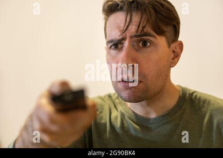 Tensed man turning the channel with a remote controller Stock Photo