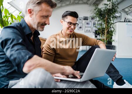 Male professional using laptop while sitting by colleague in creative office Stock Photo
