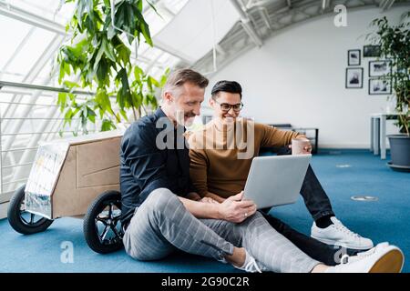 Male colleagues using laptop while sitting in creative office Stock Photo
