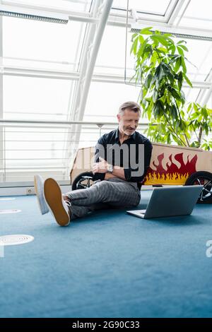 Male professional with arms crossed looking at laptop in creative office Stock Photo