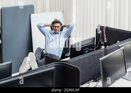 Smiling businessman with hands behind head sitting by desk Stock Photo