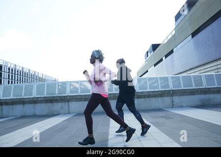 Senior woman running with man on footpath Stock Photo