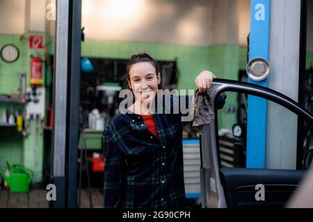 Smiling female mechanic opening car door at workshop Stock Photo