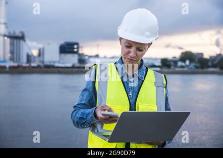 Female professional using smart phone while holding laptop Stock Photo