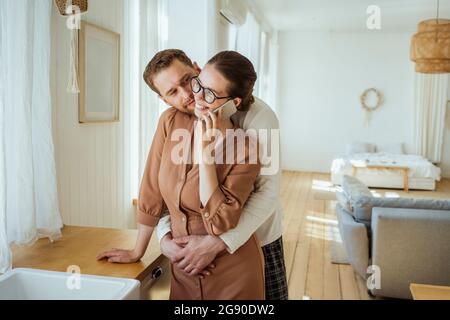 Man embracing woman talking on mobile phone at home Stock Photo